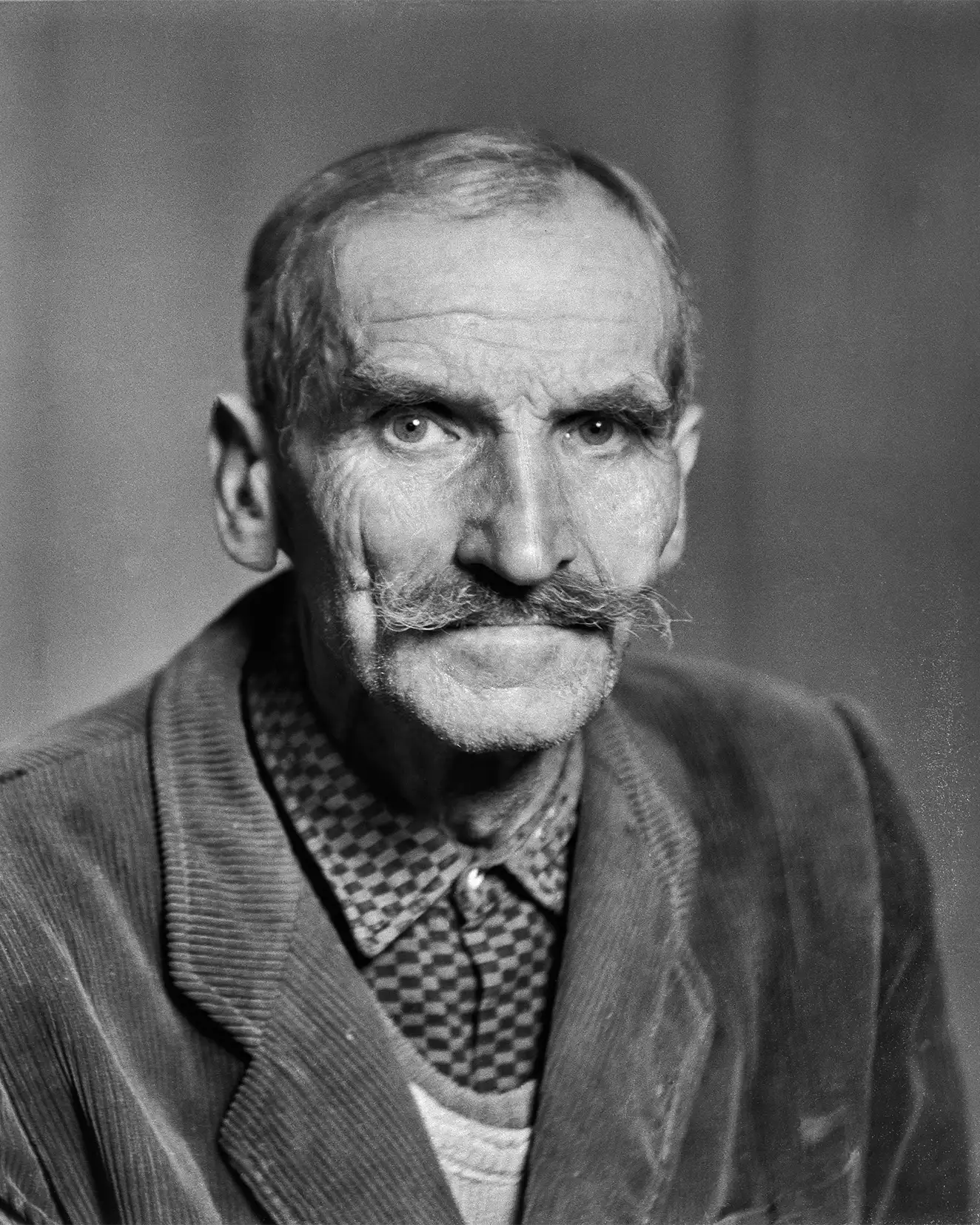 starszy mężczyzna z wąsem w koszuli w kratę i w marynarce, portret studyjny