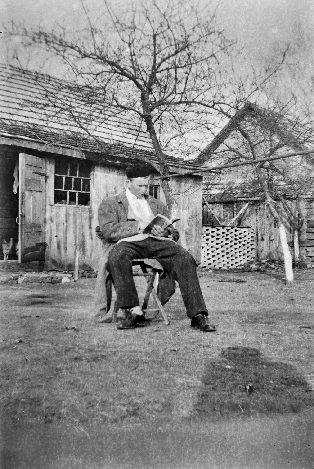 mężczyzna na krześle czytający książkę na podwórku przed drewnianą chatą