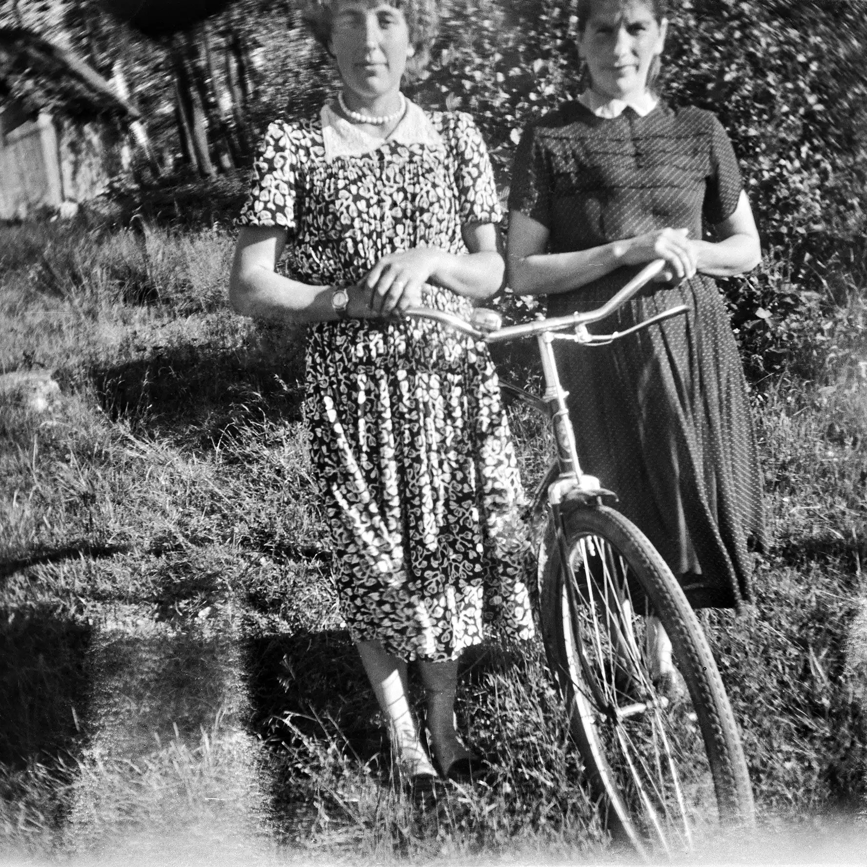 dwie kobiety w sukienkach z rowerem na łące