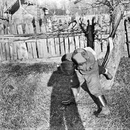 dwaj chłopcy bawiący się przed drewnianym płotem, na których widać cień fotografa