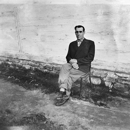 mężczyzna siedzący na krześle w ciemnej marynarce na tle drewnianej pobielonej ściany