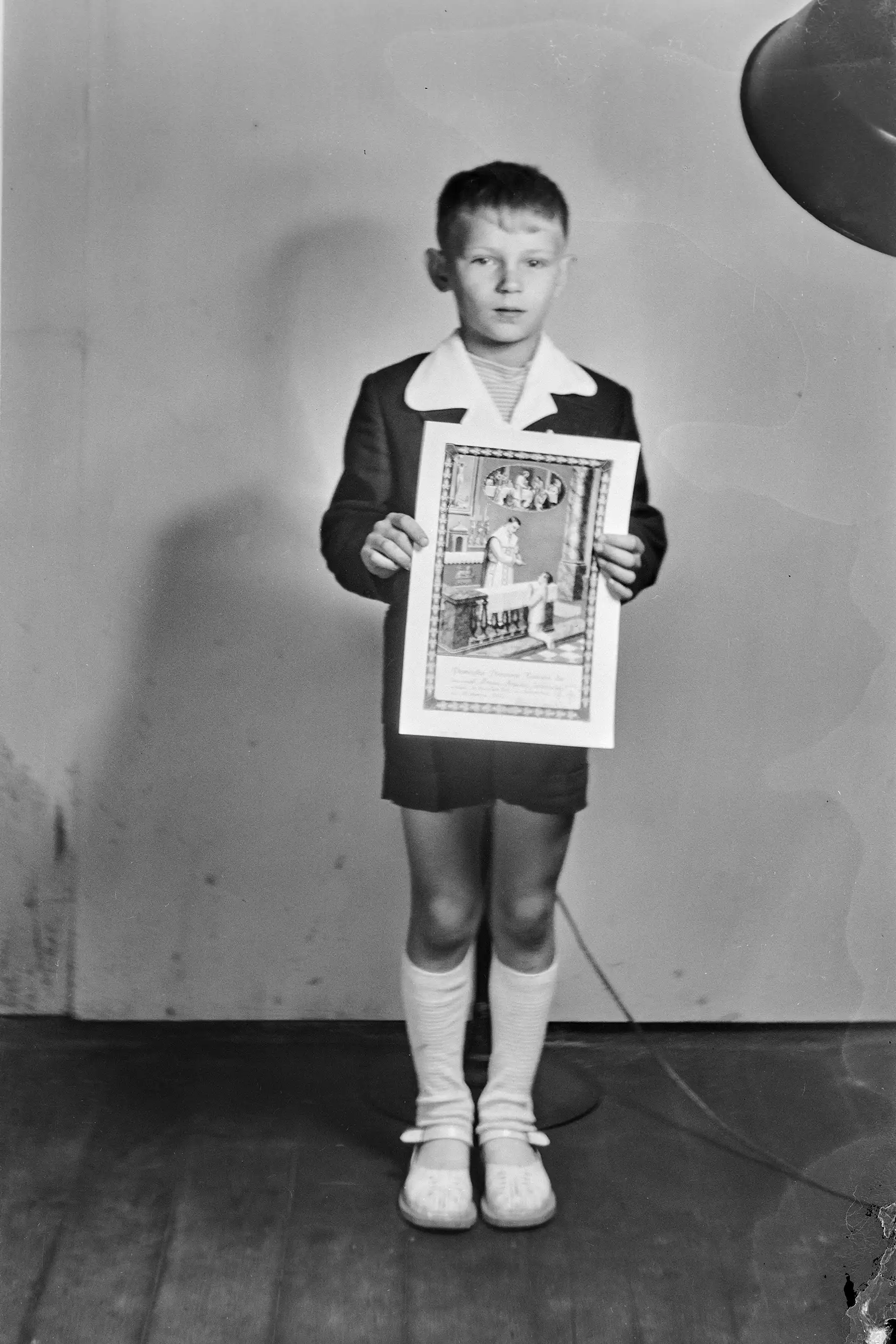 pełen pierwszokomunijny portret eleganckiego chłopca trzymającego święty obrazek